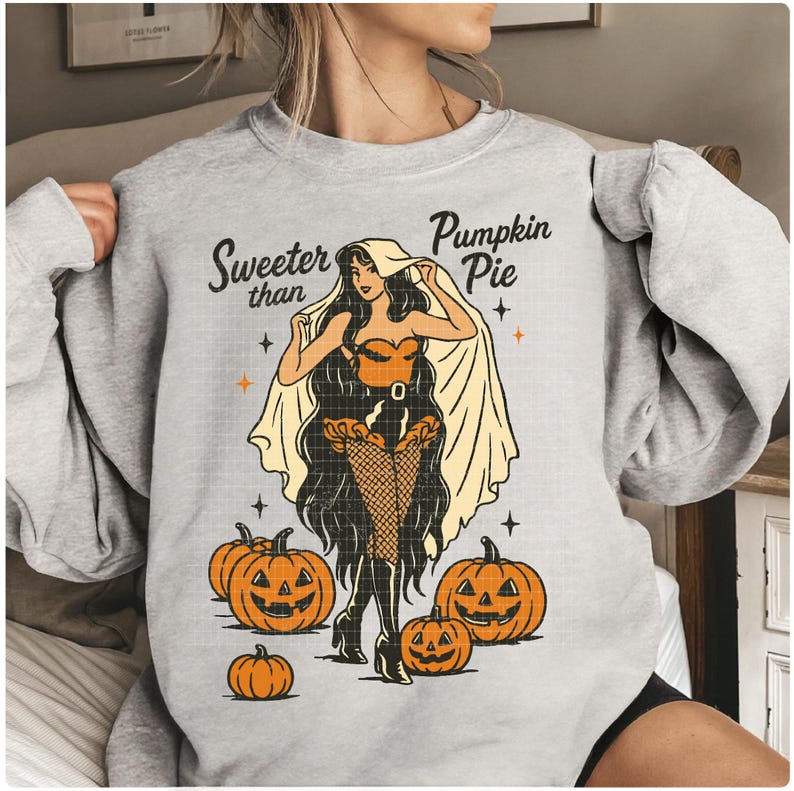Peut inclure: Un sweat-shirt gris avec un motif sur le th&egrave;me d'Halloween. Le motif repr&eacute;sente une femme de style pin-up dans une tenue couleur citrouille, entour&eacute;e de lanternes citrouilles, avec le texte "Sweeter than Pumpkin Pie".