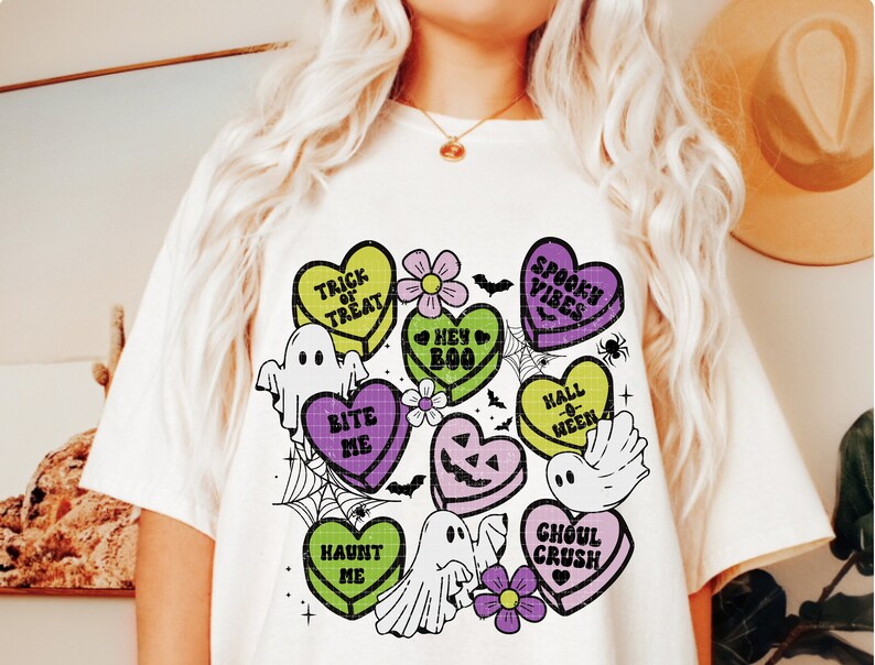 May include: A white t-shirt with a colorful graphic design of candy hearts with Halloween-themed phrases like "Trick or Treat", "Bite Me", "Spook Vibes", and "Ghoul Crush".