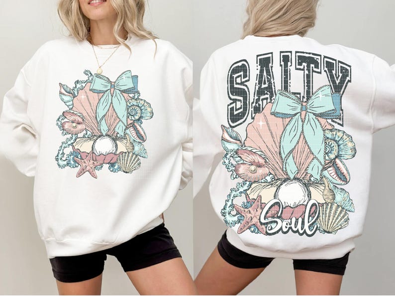 Puede incluir: Sudadera blanca con un dise&ntilde;o de concha y lazo en la parte delantera y el texto "Salty Soul" con un dise&ntilde;o de concha y lazo en la parte trasera.
