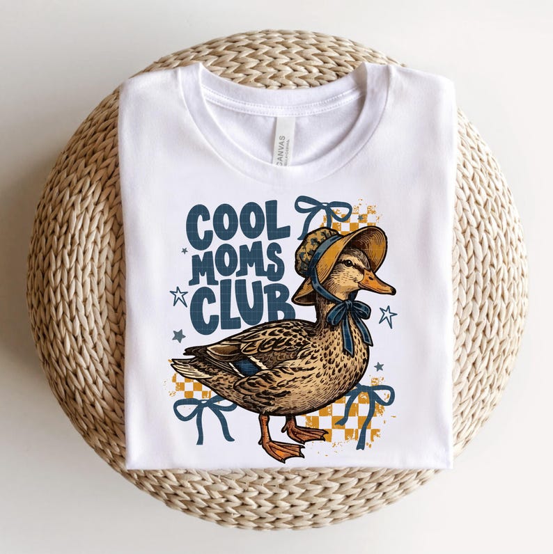 May include: White t-shirt featuring a duck wearing a bonnet and a blue bow. The text "COOL MOMS CLUB" is printed in blue with star accents. The duck is set against a yellow and white checkered background.