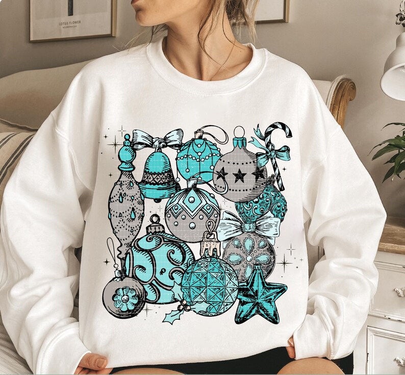 Peut inclure: Sweat-shirt blanc avec un motif d'ornements de No&euml;l repr&eacute;sentant des ornements bleus et gris avec des accents de cannes en sucre et d'&eacute;toiles.
