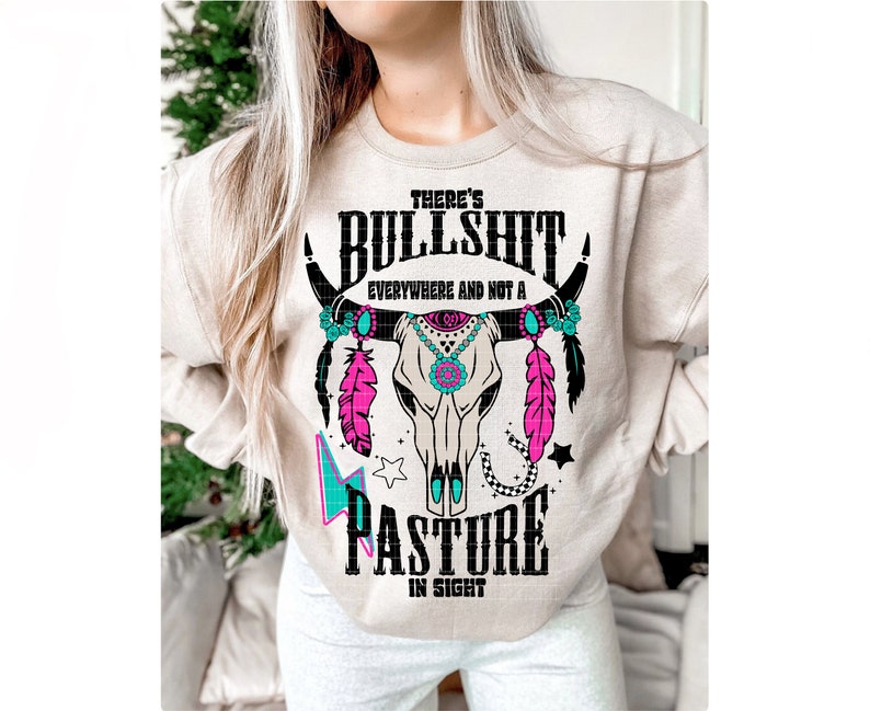 May include: A beige sweatshirt with a black and white graphic of a cow skull with turquoise and pink accents. The text "There's Bullshit Everywhere and Not a Pasture in Sight" is printed on the sweatshirt.