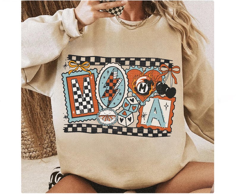 Op de afbeelding: Beige sweatshirt met een kleurrijk grafisch ontwerp. Het ontwerp bevat de letters "M" en "A" in postzegelachtige kaders, een bliksemschicht, dobbelstenen, kersen en een vlinder. Het ontwerp is omlijnd met een zwart-wit geblokt patroon.