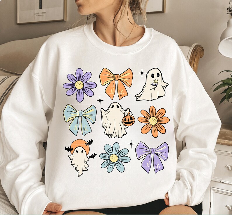 May include: White sweatshirt with a colorful Halloween design featuring ghosts, bows, and flowers. The design includes a ghost holding a pumpkin, a ghost with a flower, and a ghost with bats.