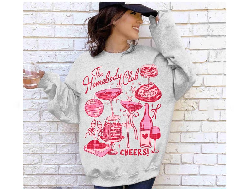 May include: A gray sweatshirt with a pink graphic design that says "The Homebody Club" and features a wine bottle, glasses, pizza, and a disco ball. The text "Cheers!" is also included in the design.