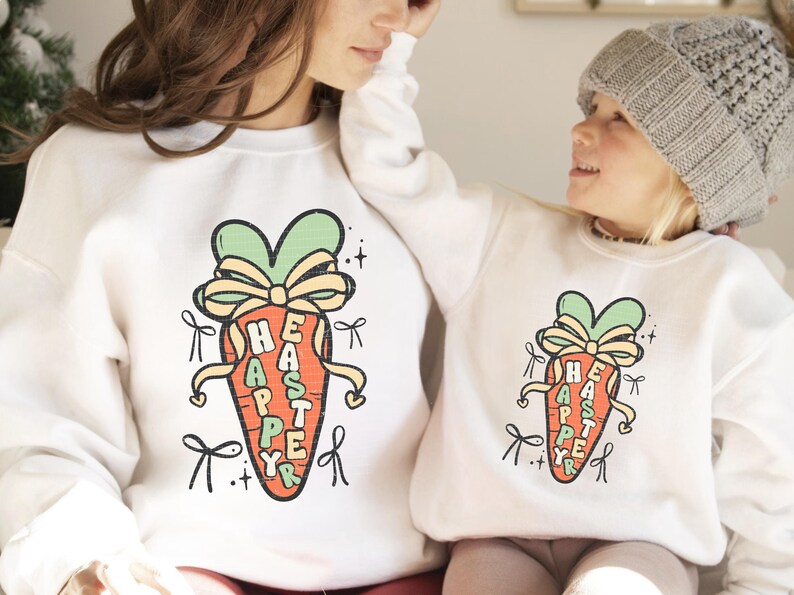 May include: White sweatshirts with a carrot graphic and the text "Happy Easter" written vertically on the carrot. The carrot is green at the top and has a yellow bow.