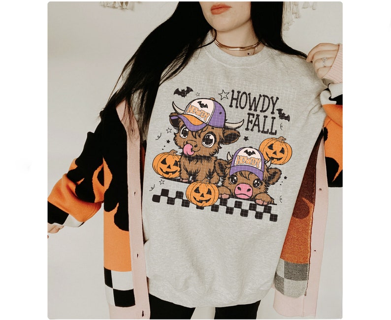 Puede incluir: Una sudadera gris con un gr&aacute;fico de dos vacas de dibujos animados que llevan sombreros y sostienen calabazas. El texto "Howdy Fall" est&aacute; impreso en la sudadera.
