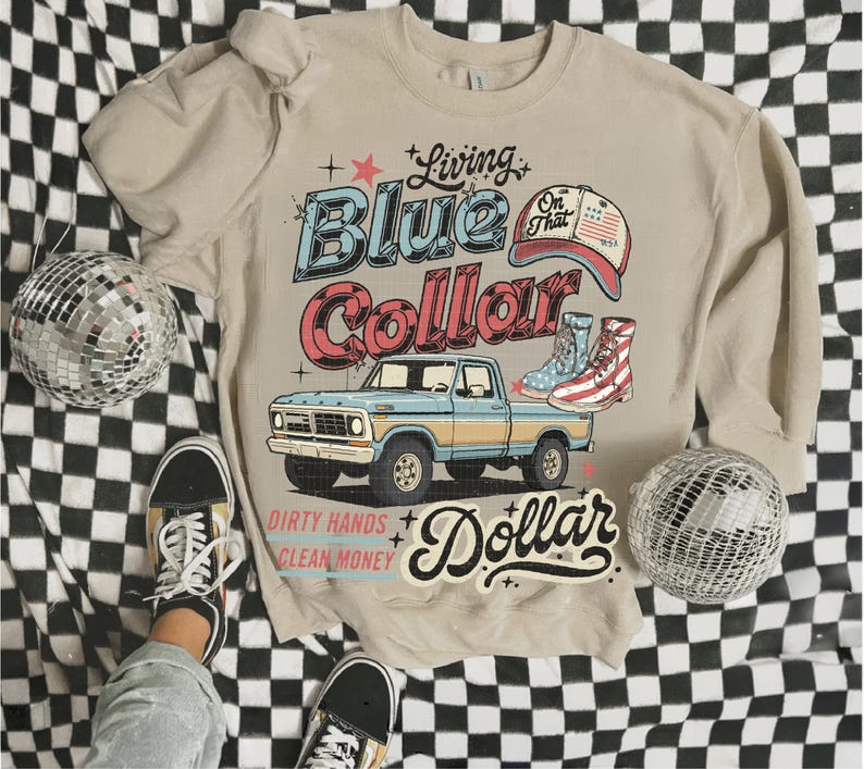 May include: Beige crewneck sweatshirt with a graphic design featuring a blue and yellow pickup truck, cowboy boots, and the text "Living Blue Collar Dollar." The design has a vintage, retro aesthetic.