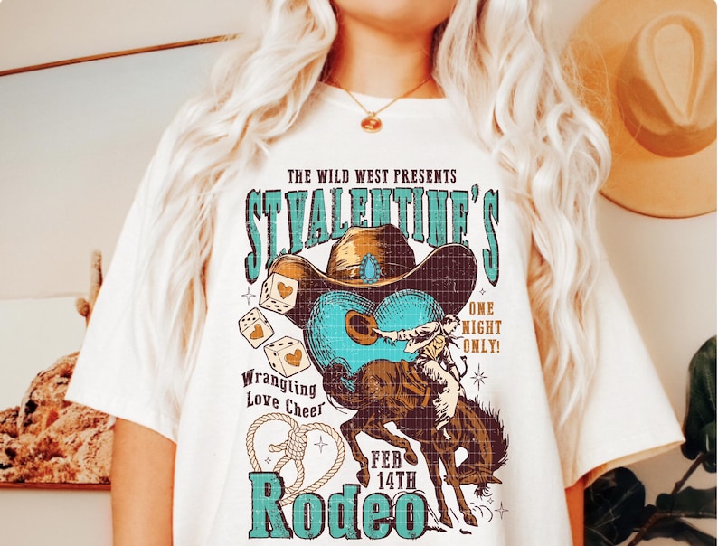 以下が含まれることがあります： ヴィンテージスタイルのグラフィックデザインが施された白いTシャツ。カウボーイが馬に乗っている様子、サイコロ、そして「The Wild West Presents St. Valentine's One Night Only! Feb 14th Rodeo」というテキストが描かれています