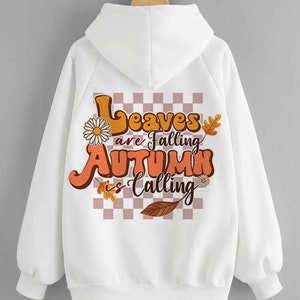 Op de afbeelding: Witte hoodie met een grafische print op de rug. De print heeft een geruite achtergrond met bladeren, bloemen en de tekst "Leaves are Falling Autumn is Calling".
