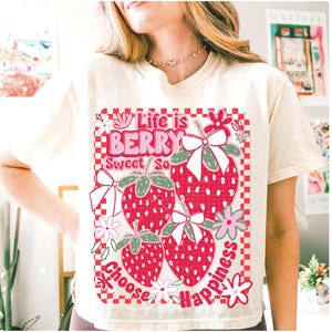 May include: A white t-shirt with a graphic of strawberries and the text "Life is Berry Sweet So Choose Happiness".