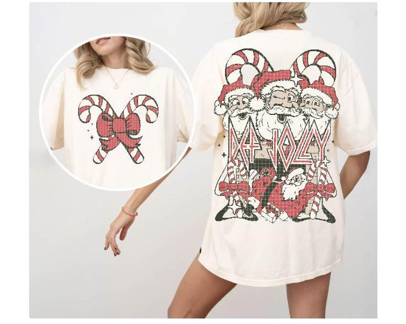 May include: A cream-colored t-shirt with a Christmas-themed graphic on the front. The graphic features three Santa Clauses with candy canes and the text "Da Jolly". The back of the shirt features a red bow with candy canes.