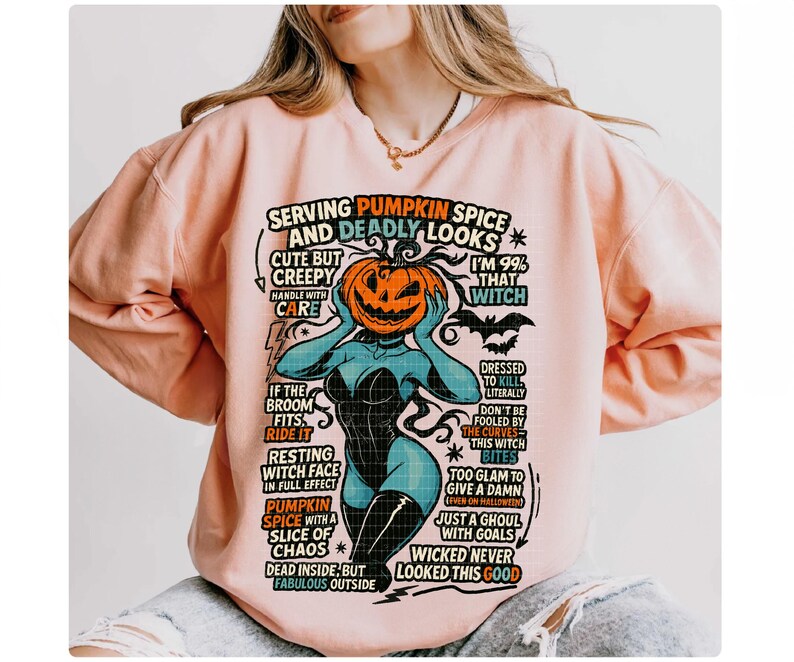 May include: A light pink sweatshirt with a graphic featuring a pumpkin-headed witch with text that reads "Serving Pumpkin Spice and Deadly Looks." The design includes phrases like "Cute but Creepy" and "Wicked Never Looked This Good."