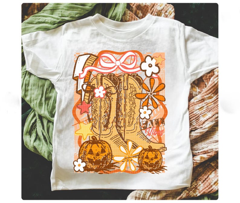 May include: White t-shirt featuring a retro-style graphic with cowboy boots, pumpkins, and flowers in shades of orange, brown, and white. The text "Fall Vibes" is also included in the design. The shirt is made of a soft material.