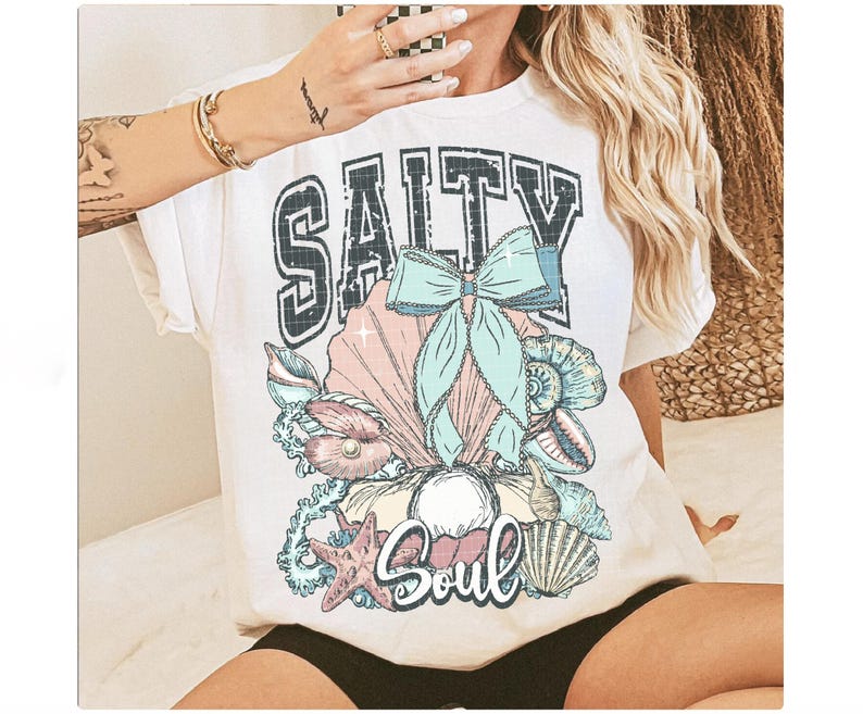 Puede incluir: Camiseta blanca con un estampado gr&aacute;fico de conchas marinas, un lazo y el texto "Salty Soul".