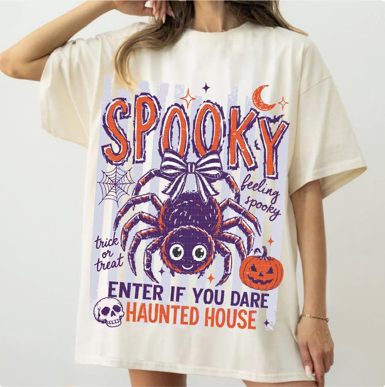 May include: An off-white t-shirt featuring a graphic print with the text SPOOKY, feeling spooky, trick or treat, ENTER IF YOU DARE, and HAUNTED HOUSE. The design includes a large spider with a bow, a pumpkin, a spiderweb, a crescent moon, and a skull.