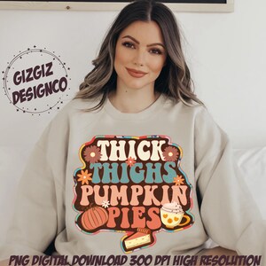 May include: A beige sweatshirt with a retro-style graphic design that says "Thick Thighs Pumpkin Pies". The graphic features a pumpkin, a cup of coffee, and a slice of pie.