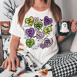 May include: A white t-shirt with a Halloween-themed design featuring candy hearts with phrases like "Trick or Treat", "Bite Me", and "Ghoul Crush". The design also includes ghosts, flowers, and a spiderweb.