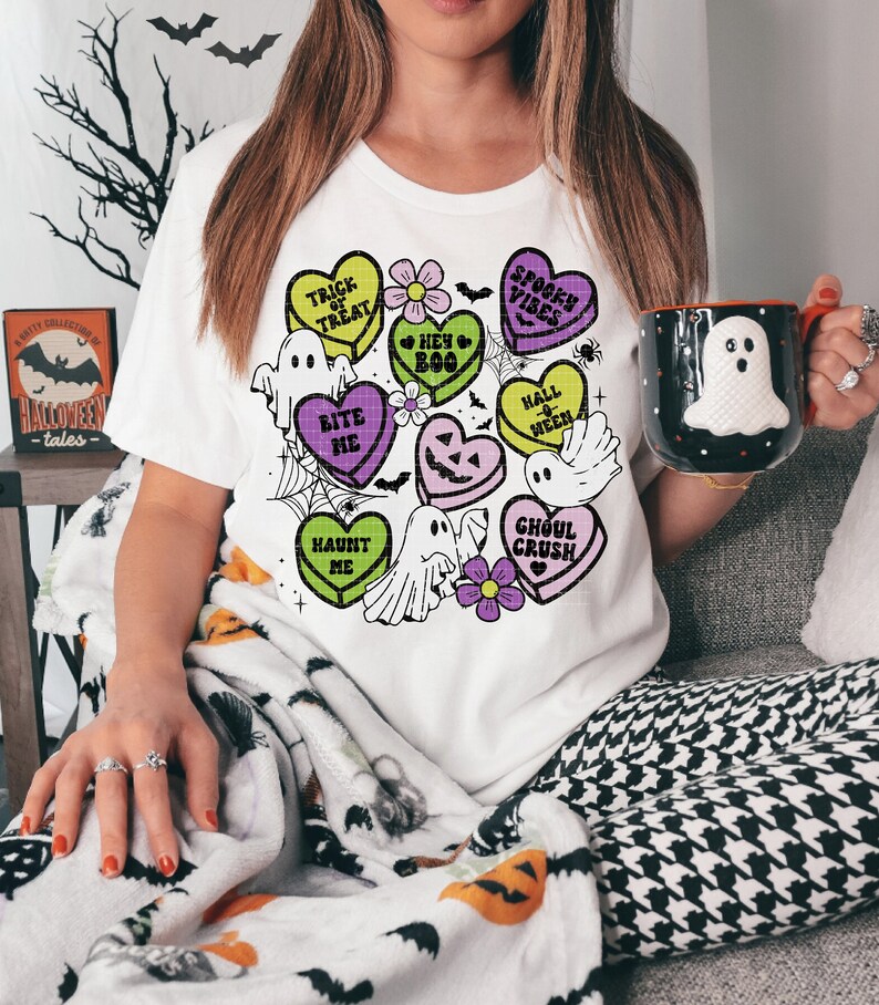 May include: A white t-shirt with a Halloween-themed design featuring candy hearts with phrases like "Trick or Treat", "Bite Me", and "Ghoul Crush". The design also includes ghosts, flowers, and a spiderweb.