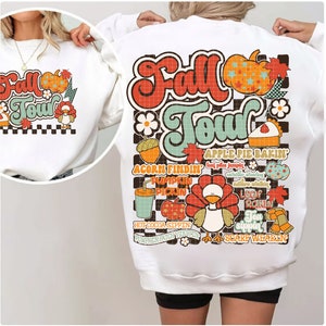 K&ouml;nnte beinhalten: Wei&szlig;er Pullover mit einem bunten Grafikdesign mit dem Text "Fall Tour" und verschiedenen Herbstmotiven, darunter ein Truthahn, K&uuml;rbisse, Bl&auml;tter und eine Torte.