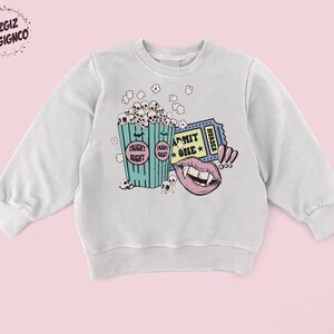 May include: A light gray sweatshirt with a graphic print of a bucket of popcorn with skulls, a ticket that says "Admit One" and "Murder", and a vampire mouth with fangs.