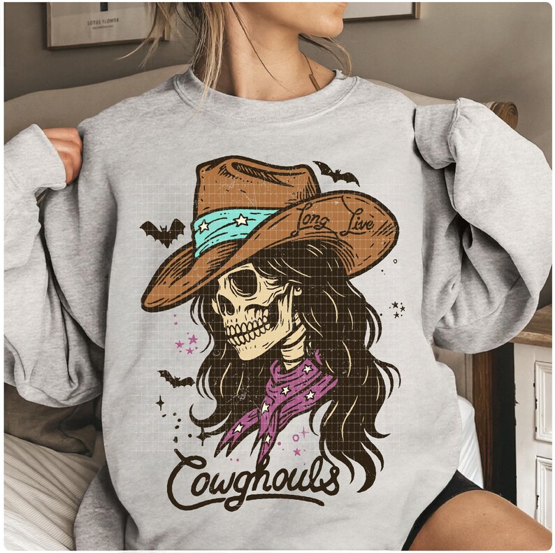 May include: A light gray sweatshirt featuring a graphic of a skull wearing a cowboy hat with the text "Long Live" and "Cowghouls". The hat is brown with a turquoise band and stars. The skull has long brown hair and a purple bandana.