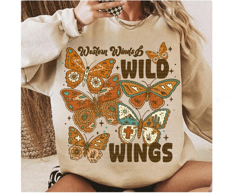 以下が含まれることがあります： ベージュのスウェットシャツ。蝶のグラフィックと「Western Winds & Wild Wings」の文字入り。蝶はオレンジ、茶色、ターコイズ色で、花柄と幾何学模様が施されています。スウェットシャツはクルーネックと長袖です。