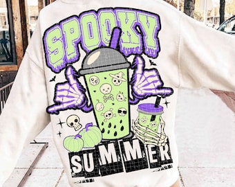 May include: White sweatshirt with a green and purple graphic of a spooky summer drink with skulls and crossbones. The text "Spooky Summer" is printed on the sweatshirt.