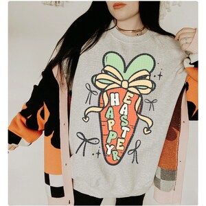 May include: A gray sweatshirt with a cartoon carrot wearing a bow and the text "Happy Easter" on it. The sweatshirt is being worn by a person with long dark hair.