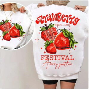 May include: White sweatshirt with a red and green strawberry graphic and the text "Strawberry Festival A berry good time" and "EST. 1968".
