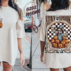 Puede incluir: Una camiseta blanca de gran tama&ntilde;o con un estampado gr&aacute;fico de esqueletos sosteniendo calabazas. La parte posterior de la camiseta tiene un estampado gr&aacute;fico m&aacute;s grande de esqueletos sosteniendo calabazas con el texto "Stay Spooky".