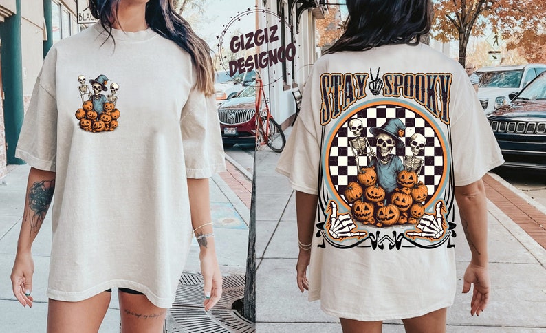 Puede incluir: Una camiseta blanca de gran tama&ntilde;o con un estampado gr&aacute;fico de esqueletos sosteniendo calabazas. La parte posterior de la camiseta tiene un estampado gr&aacute;fico m&aacute;s grande de esqueletos sosteniendo calabazas con el texto "Stay Spooky".