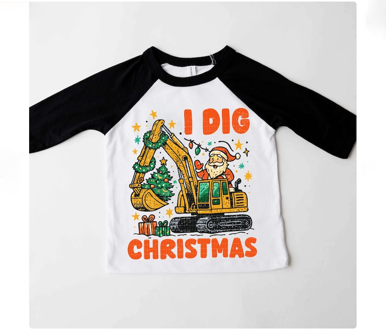 May include: White and black raglan-style shirt with a colorful graphic. The graphic features a yellow excavator with Santa Claus in the driver's seat, a Christmas tree, and the text "I DIG CHRISTMAS" in orange.