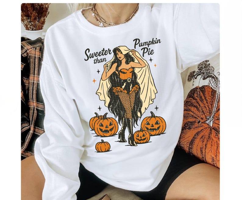 Peut inclure: Sweat-shirt blanc &agrave; manches longues avec un motif d'Halloween. Le motif repr&eacute;sente une femme en costume, des citrouilles et le texte "Sweeter than Pumpkin Pie". La femme porte un corset, des bas r&eacute;sille et une cape.