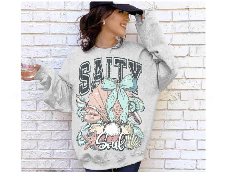 Puede incluir: Sudadera gris con un gr&aacute;fico de conchas marinas y un lazo, y el texto "Salty Soul".
