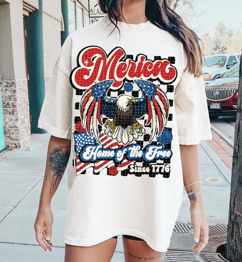 May include: White t-shirt with a red, white, and blue graphic design featuring an eagle, American flags, and the text "Merica Home of the Free Since 1776".