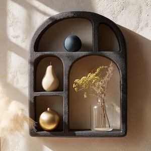 May include: Black arched wall shelf with five compartments. The shelf is decorated with a blue sphere, a pear-shaped object, a gold sphere, and a glass vase with dried flowers.