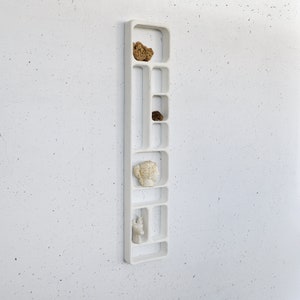 May include: White wall-mounted shelf unit with multiple rectangular compartments. The shelf is empty except for a few small decorative items.