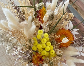Può includere: Un bouquet di fiori secchi con un mix di fiori bianchi, gialli e arancioni. Il bouquet comprende erbe secche e erba della pampa bianca e soffice.