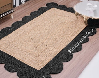 May include: A natural fiber rug with a black border and scalloped edges. The rug is laid out on a hardwood floor in a living room setting.