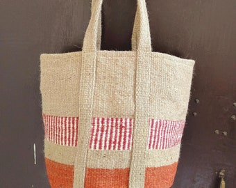 May include: A beige tote bag with red and white striped fabric accents and orange fabric accents. The bag is made of woven fabric and has two long straps.