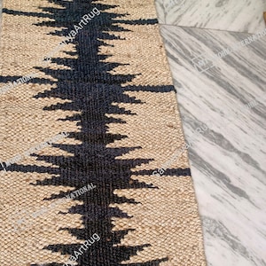 May include: A black and beige jute rug with a geometric pattern. The rug is made from natural fibres and has a textured surface.