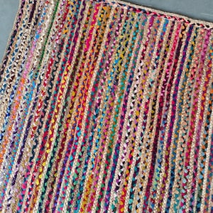 以下が含まれることがあります： 鮮やかなマルチカラーのデザインの長方形ジュートラグ。ラグは、赤、青、黄、緑の色合いのカラフルな織りセクションと交互に配置された、天然ジュートの垂直ストライプが特徴です。エッジは、編み込みのボーダーで丁寧に仕上げられています。