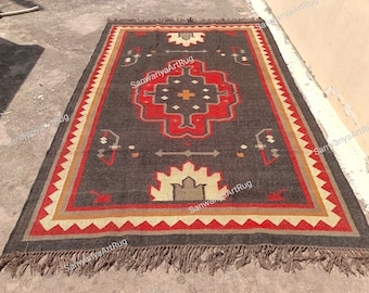 May include: A dark gray, red, and beige handwoven rug with a geometric pattern. The rug has a fringe border and is made of natural fibers.