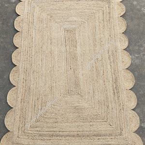 May include: A natural fiber rug with a scalloped edge. The rug is made of woven jute and has a light brown color.