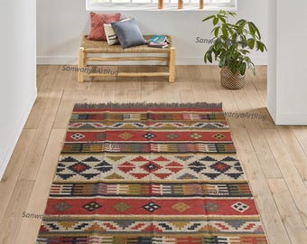 May include: A colorful, handwoven rug with geometric patterns in shades of red, blue, green, and beige. The rug has a fringed edge and is made of natural fibers.