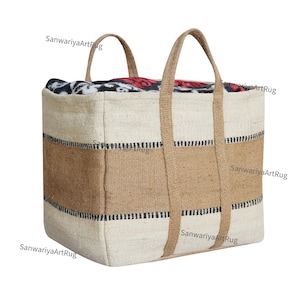May include: A large, rectangular, woven storage tote bag with brown and white stripes and black accents. The bag has two thick, woven handles and is made of natural fibers. The bag is filled with a colorful blanket.