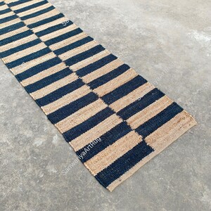 May include: A black and natural jute rug with a striped pattern. The rug is laid out on a concrete floor.