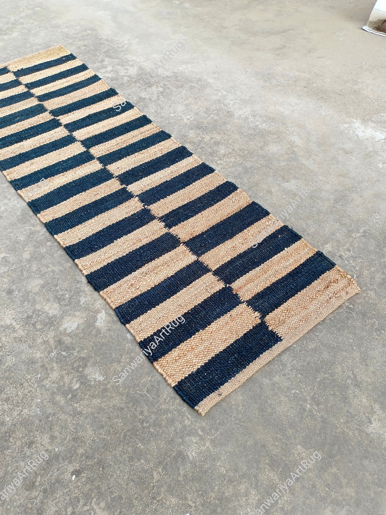 May include: A black and natural jute rug with a striped pattern. The rug is laid out on a concrete floor.