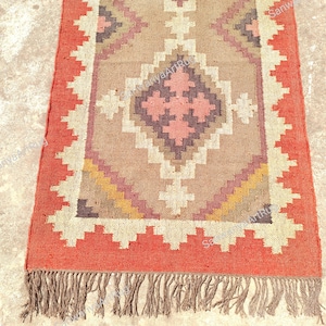 May include: A red and brown patterned rug with fringe. The rug has a geometric design with a central diamond shape.